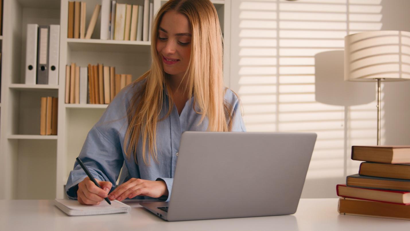 Persoana care noteaza referinte bibliografice într-un caiet lânga un laptop